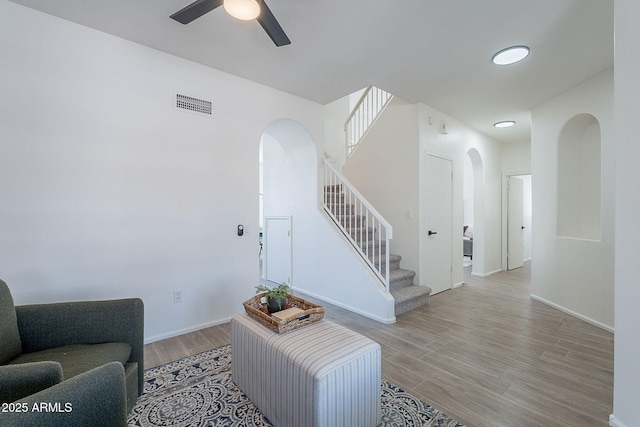 living room featuring a ceiling fan, visible vents, stairs, wood finished floors, and arched walkways