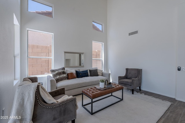living area with a wealth of natural light, visible vents, a high ceiling, and wood finished floors