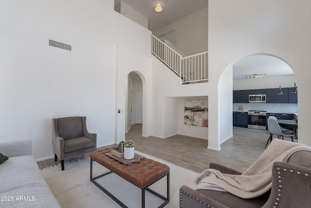 living area with light wood-style flooring, a high ceiling, visible vents, baseboards, and arched walkways