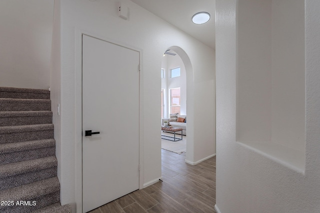 staircase featuring arched walkways, baseboards, and wood finished floors