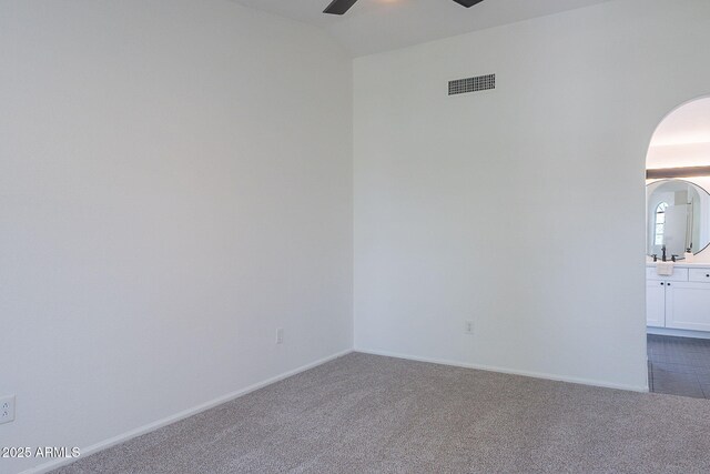 unfurnished room featuring arched walkways, ceiling fan, dark carpet, and visible vents