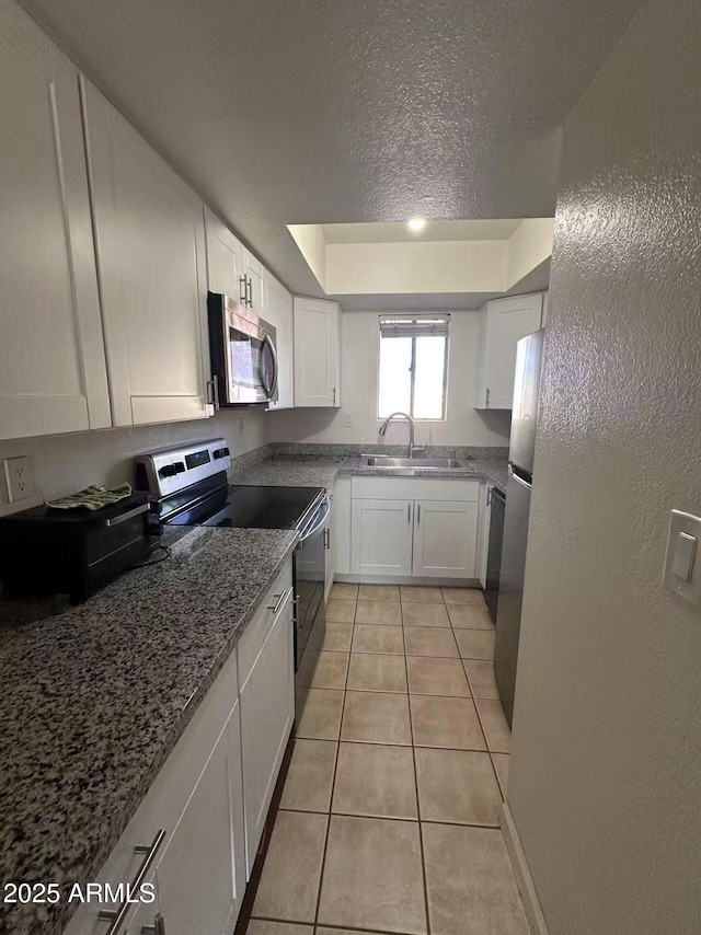 kitchen with appliances with stainless steel finishes, sink, white cabinets, dark stone counters, and light tile patterned floors