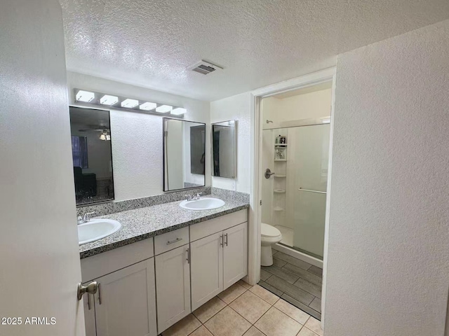 bathroom with a shower with door, vanity, a textured ceiling, tile patterned floors, and toilet