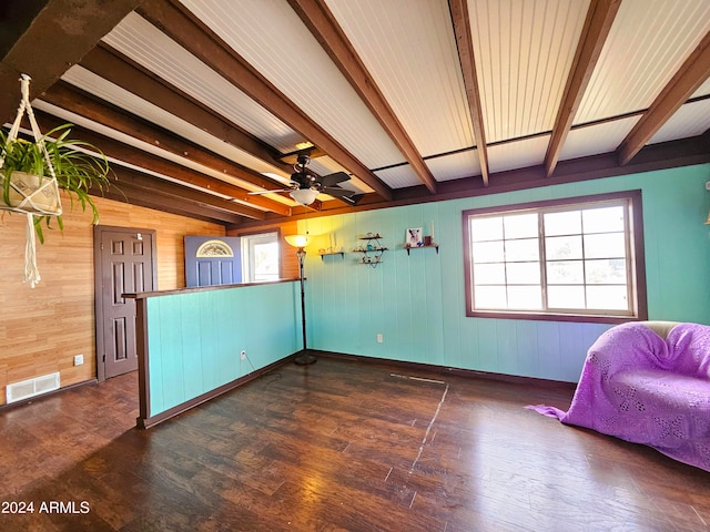 unfurnished room featuring lofted ceiling with beams, ceiling fan, dark wood-type flooring, and wood walls