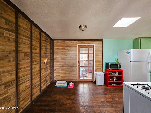 kitchen with a textured ceiling, white appliances, a skylight, and wooden walls