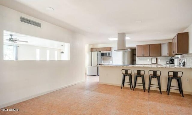 kitchen featuring ceiling fan, white refrigerator, island exhaust hood, kitchen peninsula, and a kitchen bar