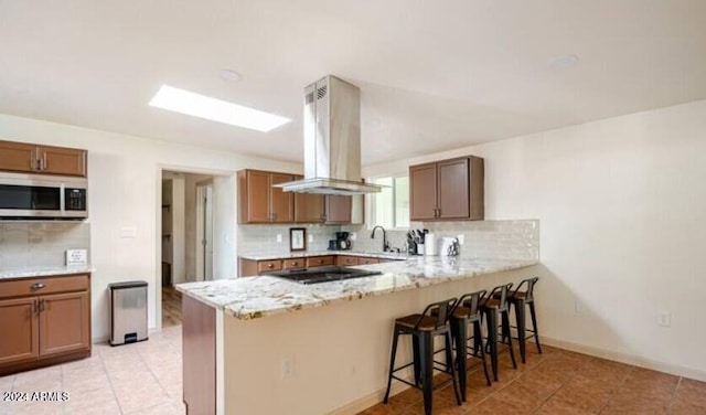 kitchen featuring backsplash, black electric stovetop, a kitchen breakfast bar, kitchen peninsula, and island exhaust hood