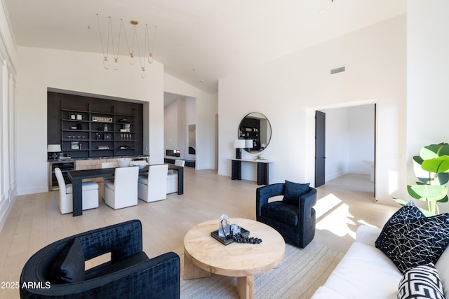 living area featuring light wood-style flooring, visible vents, and high vaulted ceiling