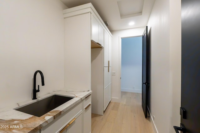 kitchen with light stone countertops, visible vents, a sink, white cabinetry, and light wood-type flooring