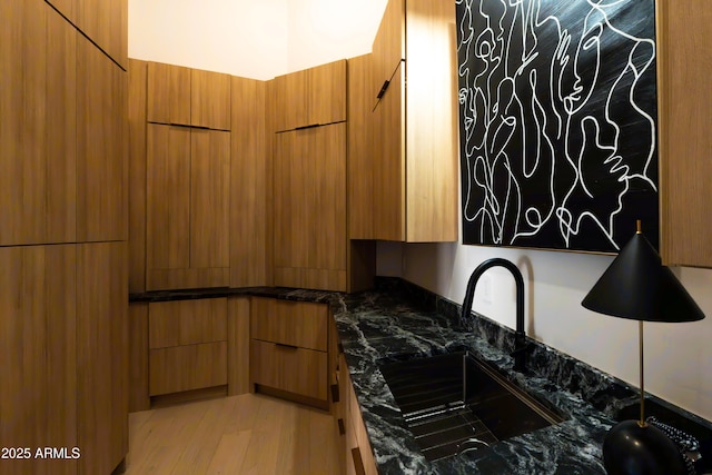 kitchen with a sink, modern cabinets, dark stone countertops, and brown cabinetry