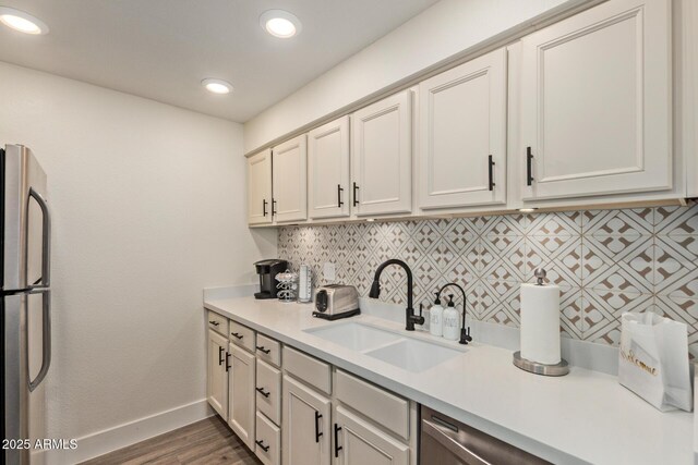 kitchen featuring a sink, light countertops, freestanding refrigerator, tasteful backsplash, and baseboards