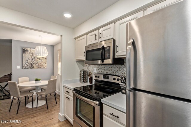 kitchen featuring appliances with stainless steel finishes, tasteful backsplash, light wood-type flooring, light countertops, and white cabinetry