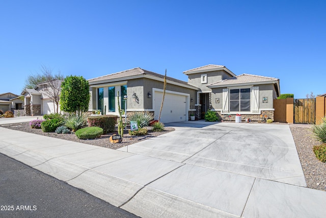 prairie-style home featuring fence, stucco siding, concrete driveway, a garage, and stone siding