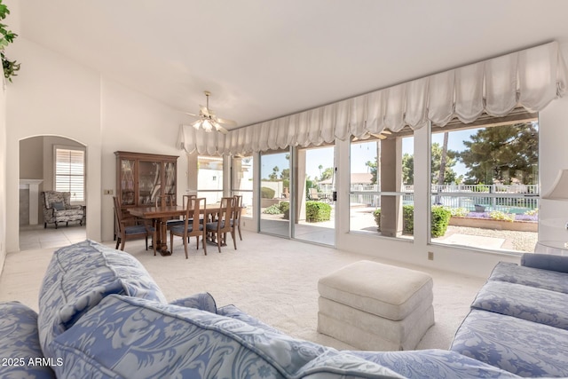 living area with light colored carpet, arched walkways, ceiling fan, and vaulted ceiling