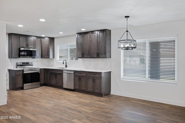 kitchen with pendant lighting, sink, stainless steel appliances, wood-type flooring, and decorative backsplash