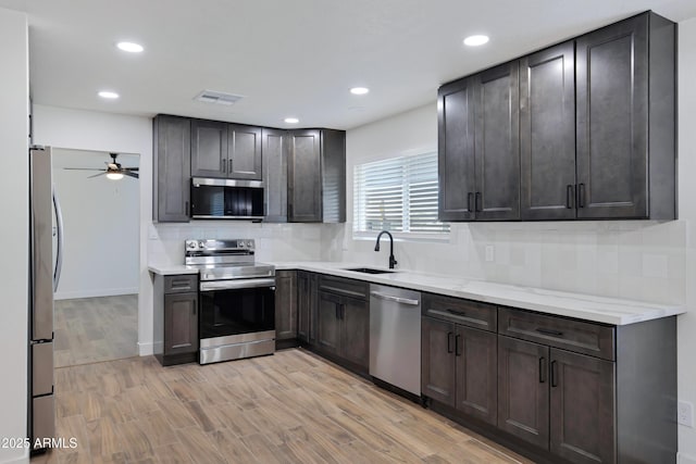 kitchen with appliances with stainless steel finishes, sink, decorative backsplash, dark brown cabinetry, and light hardwood / wood-style floors