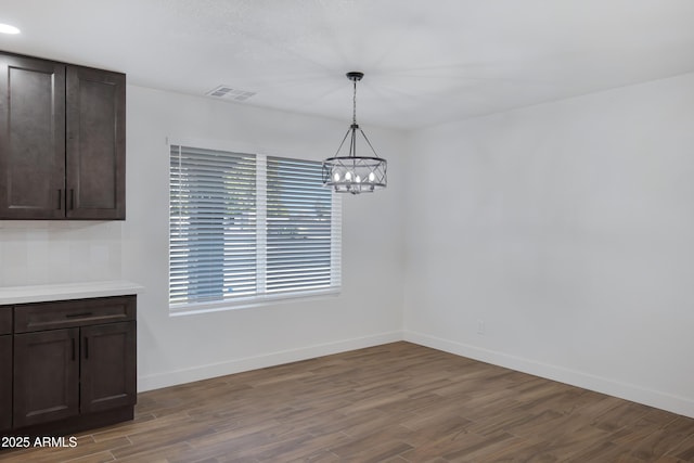 unfurnished dining area featuring dark wood-type flooring and a chandelier