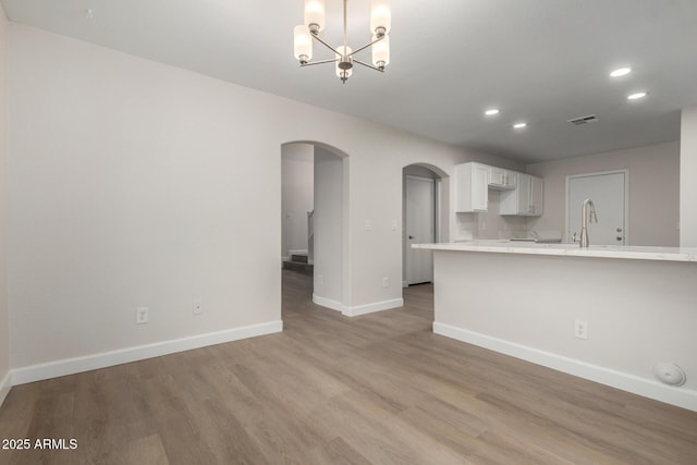 unfurnished living room featuring visible vents, baseboards, recessed lighting, light wood-style floors, and arched walkways