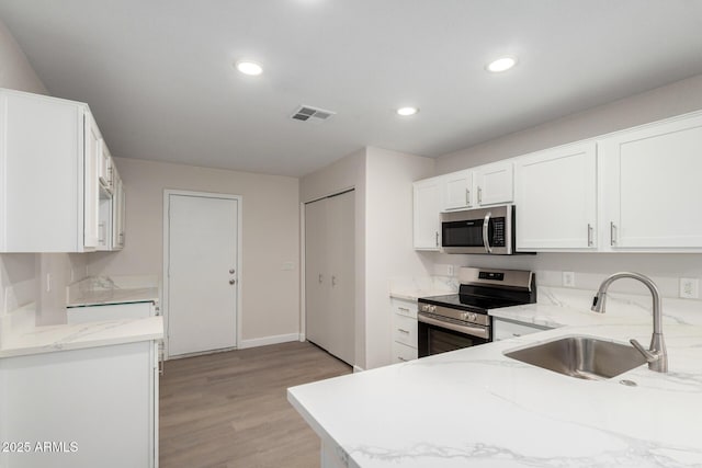 kitchen featuring light stone countertops, visible vents, a sink, appliances with stainless steel finishes, and white cabinetry