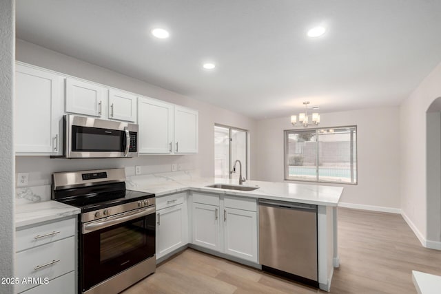 kitchen with appliances with stainless steel finishes, a peninsula, an inviting chandelier, white cabinets, and a sink