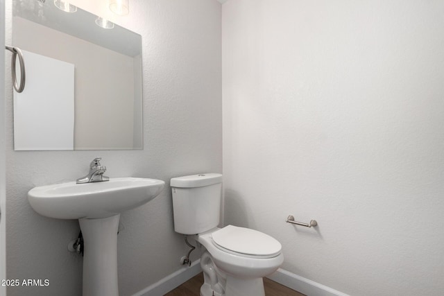 half bathroom featuring baseboards, toilet, and wood finished floors