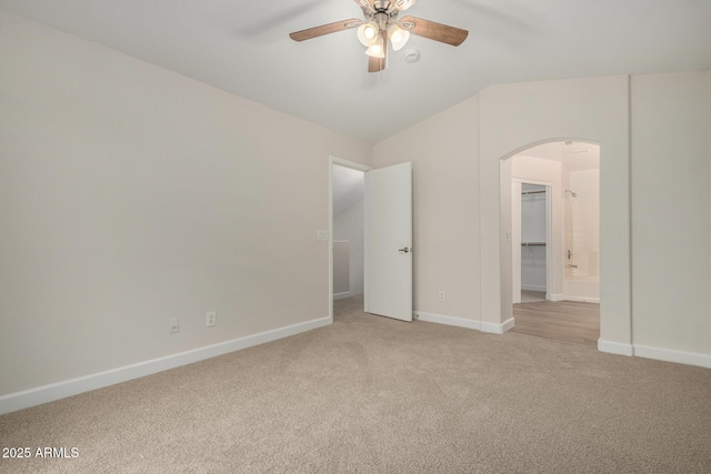 unfurnished bedroom featuring arched walkways, light colored carpet, baseboards, and vaulted ceiling