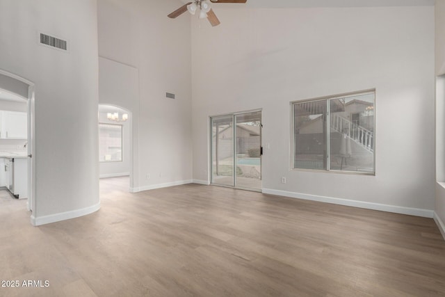 unfurnished living room with visible vents, light wood-style flooring, ceiling fan with notable chandelier, arched walkways, and baseboards