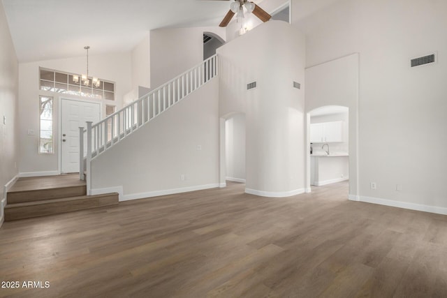 unfurnished living room with visible vents, ceiling fan with notable chandelier, wood finished floors, arched walkways, and baseboards