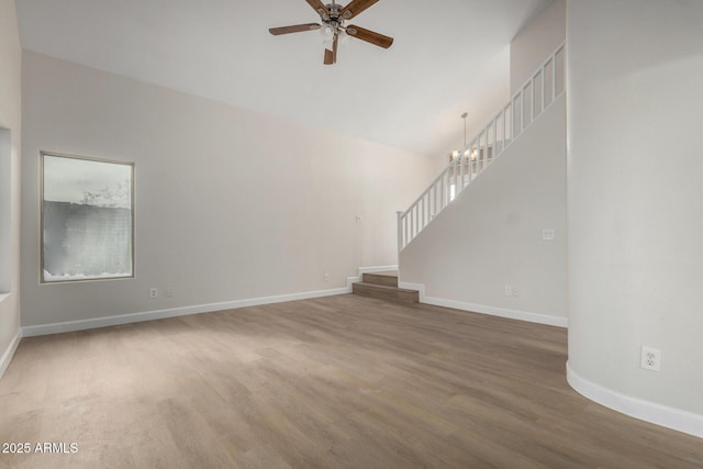 unfurnished living room featuring baseboards, stairway, ceiling fan with notable chandelier, wood finished floors, and high vaulted ceiling