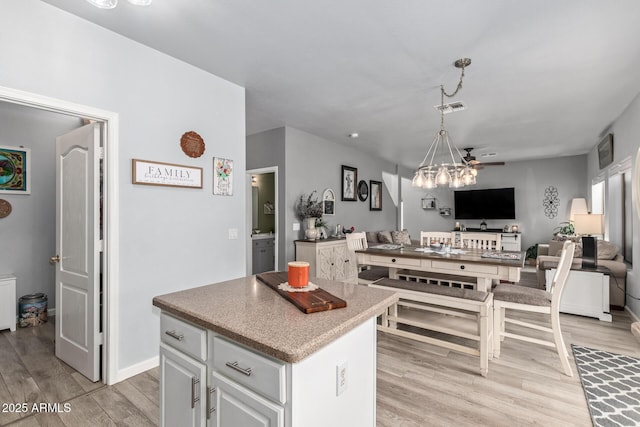 kitchen featuring white cabinets, ceiling fan, light wood-type flooring, decorative light fixtures, and a kitchen island