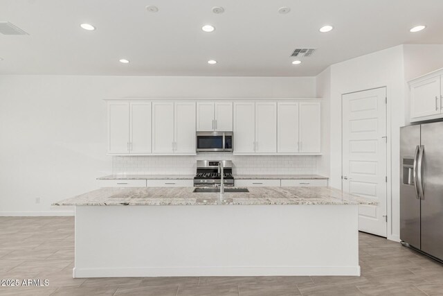 19151 W Coolidge St, Litchfield Park, AZ 85340 - kitchen with appliances with stainless steel finishes, a sink, an island with sink, decorative backsplash, and white cabinets
