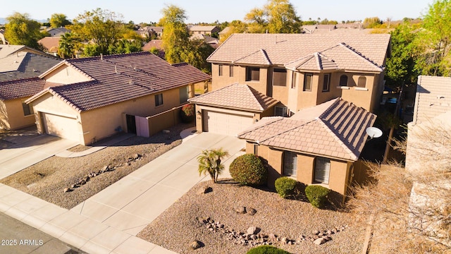 view of front of property featuring an attached garage, driveway, a tiled roof, a residential view, and stucco siding