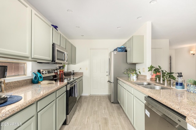 kitchen with sink, stainless steel appliances, light hardwood / wood-style floors, and light stone countertops