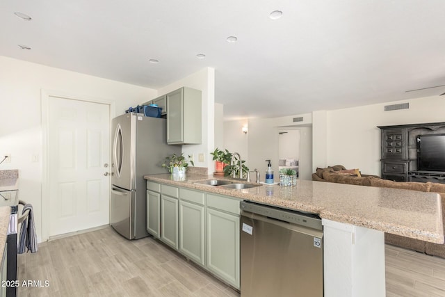 kitchen featuring stainless steel appliances, sink, green cabinets, light wood-type flooring, and kitchen peninsula