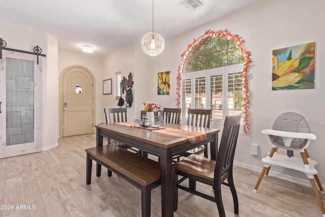 dining space with a notable chandelier, a barn door, and light hardwood / wood-style flooring