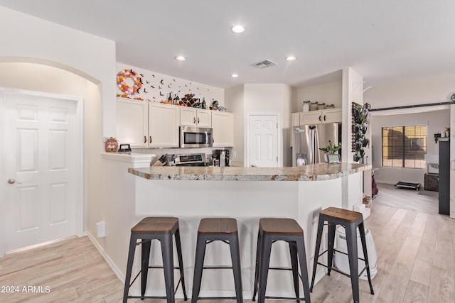 kitchen featuring a breakfast bar, light stone counters, stainless steel appliances, and light hardwood / wood-style floors