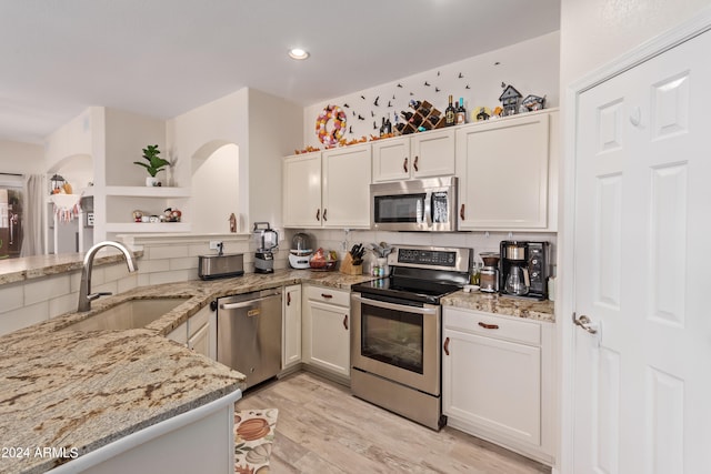 kitchen with light stone counters, appliances with stainless steel finishes, white cabinetry, light hardwood / wood-style floors, and sink