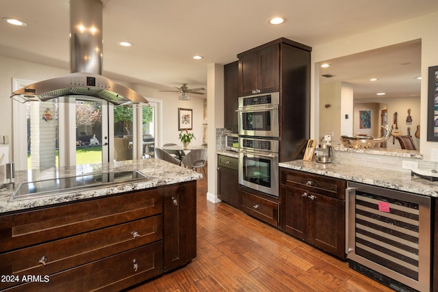 kitchen with wine cooler, stainless steel double oven, light stone counters, and dark hardwood / wood-style flooring