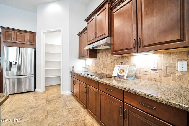 kitchen featuring stainless steel fridge, black electric stovetop, light stone counters, and decorative backsplash