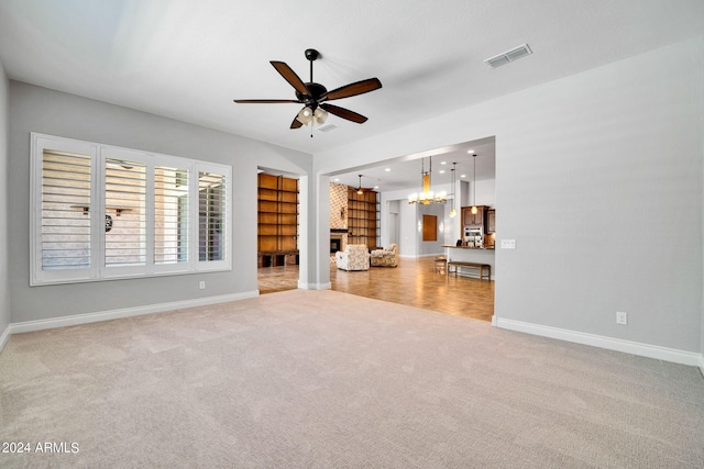 unfurnished living room with ceiling fan with notable chandelier, light colored carpet, and a fireplace