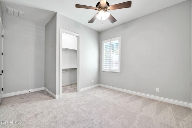 unfurnished bedroom with a walk in closet, ceiling fan, light colored carpet, and a closet