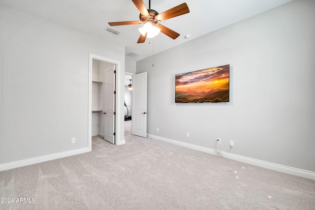 unfurnished bedroom with a closet, ceiling fan, a spacious closet, and light carpet