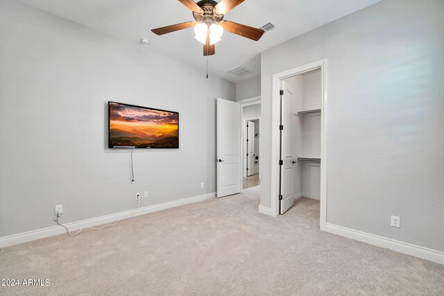 unfurnished bedroom featuring light colored carpet, ceiling fan, a walk in closet, and a closet