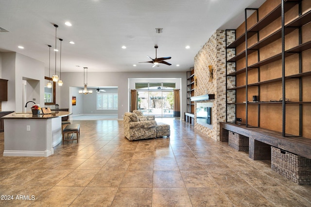 unfurnished living room with a large fireplace, ceiling fan with notable chandelier, and sink