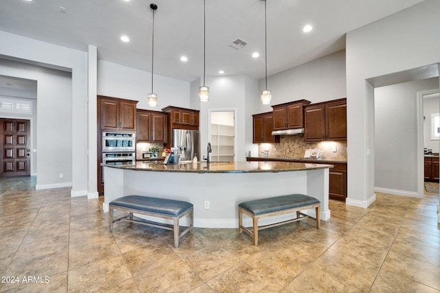 kitchen featuring appliances with stainless steel finishes, a large island with sink, a kitchen breakfast bar, dark stone counters, and pendant lighting