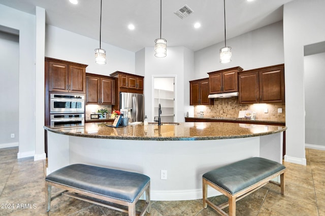 kitchen featuring hanging light fixtures, appliances with stainless steel finishes, a spacious island, a kitchen bar, and tasteful backsplash