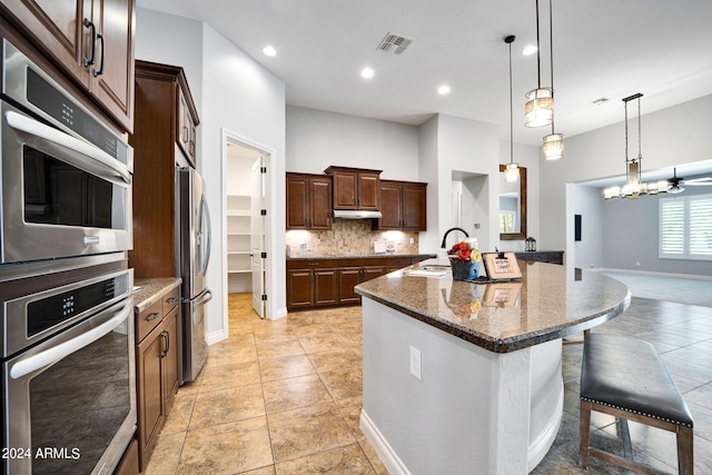 kitchen with a kitchen breakfast bar, pendant lighting, backsplash, an island with sink, and stainless steel appliances