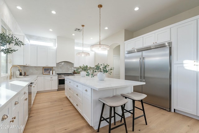 kitchen featuring sink, premium range hood, white cabinetry, high end appliances, and a kitchen island