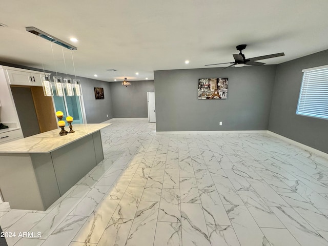 kitchen with ceiling fan, decorative light fixtures, light stone countertops, white cabinets, and a center island