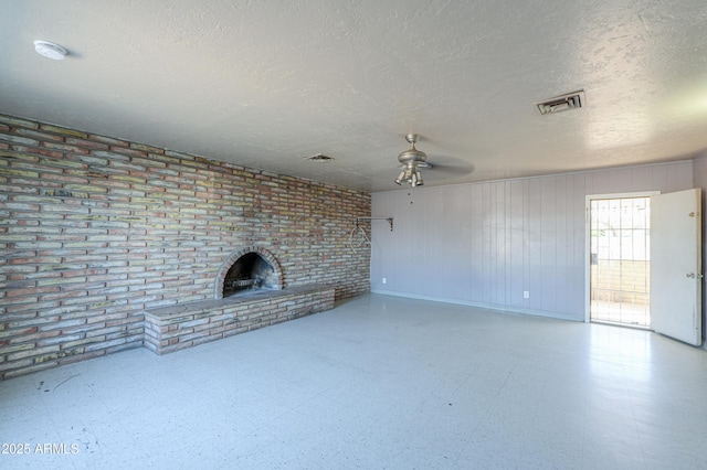 unfurnished living room featuring a brick fireplace, brick wall, ceiling fan, and a textured ceiling